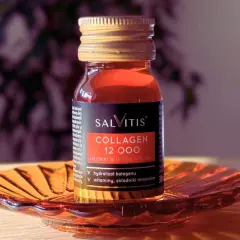 Szklana buteleczka suplementu diety SALVITIS Collagen 12 000, z płynem o bursztynowym kolorze, stoi na ozdobnej, pomarańczowej podstawce.