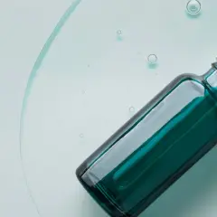 Szklana buteleczka z pipetką, zawierająca serum z kwasem mlekowym, unosząca się w przejrzystej cieczy z bąbelkami.