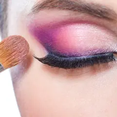 Pędzel do makijażu tworzy wyrazisty **cut crease** na powiece, podkreślając oko intensywnym fioletem i różem.