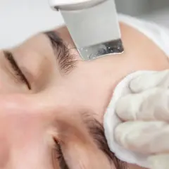 Zabieg oczyszczania twarzy: **peeling kawitacyjny** usuwa martwy naskórek, a wacik kosmetyczny delikatnie osusza skórę.