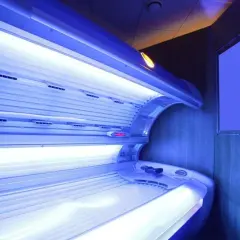 Wnętrze solarium z łóżkiem do opalania. Jasne lampy emitują niebieskie światło, tworząc atmosferę relaksu i przygotowania do letniego okresu.