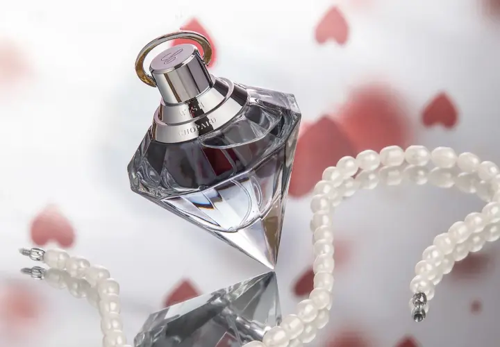 Luksusowy flakon ambperfumy Chopard Wish, otoczony perłami i serduszkami, symbolizuje elegancję i romantyzm.
