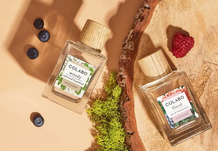 Dwa flakony perfum COLABO: "woody" z jagodami i "floral" z maliną, otoczone mchem i drewnem.