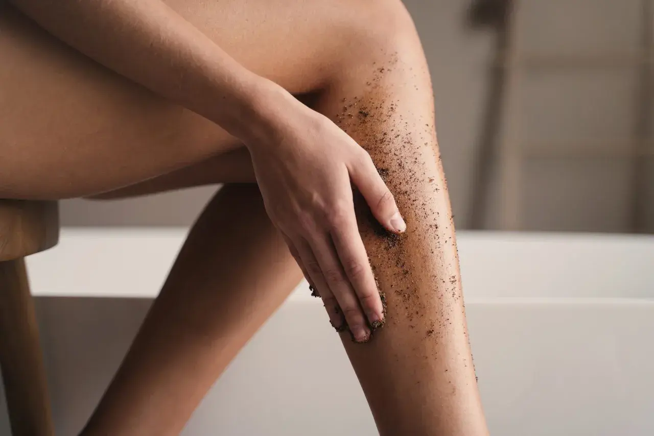 Kobieta wykonuje peeling kawowy na nogach, przygotowując skórę do golenia.