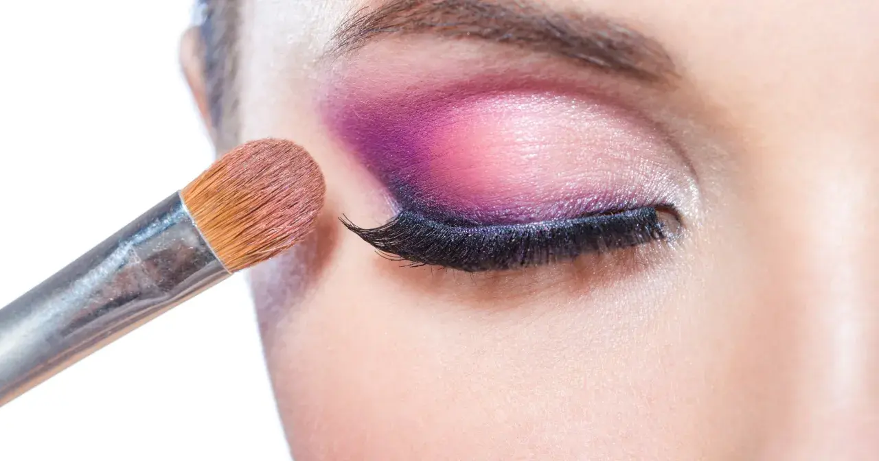 Pędzel do makijażu tworzy wyrazisty **cut crease** na powiece, podkreślając oko intensywnym fioletem i różem.