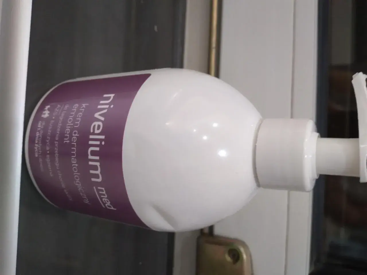 Biała butelka z pompką, na której widnieje napis "nivelium med krem dermatologiczny".