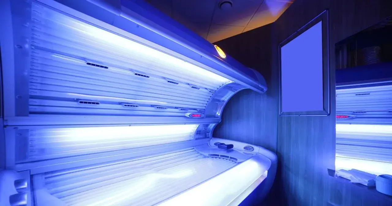 Wnętrze solarium z łóżkiem do opalania. Jasne lampy emitują niebieskie światło, tworząc atmosferę relaksu i przygotowania do letniego okresu.