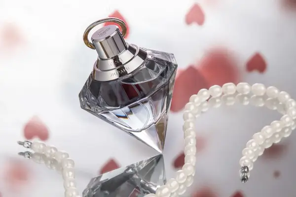 Luksusowy flakon ambperfumy Chopard Wish, otoczony perłami i serduszkami, symbolizuje elegancję i romantyzm.